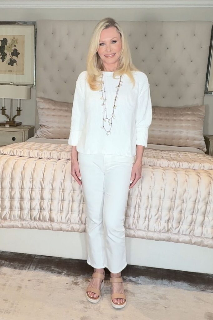 Fashion infleucner for women over 60 wearing a white fisherman sweater with white kick flare jeans as an example of Affordable ageless fashion for women over 50.